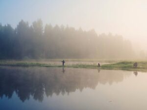 Dimhöljd sjö med tre personer som fiskar i morgonljuset