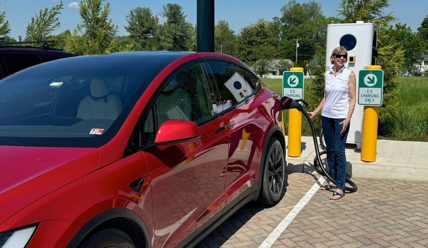 En kvinna laddar en röd elbil vid en laddstation på landsbygden.